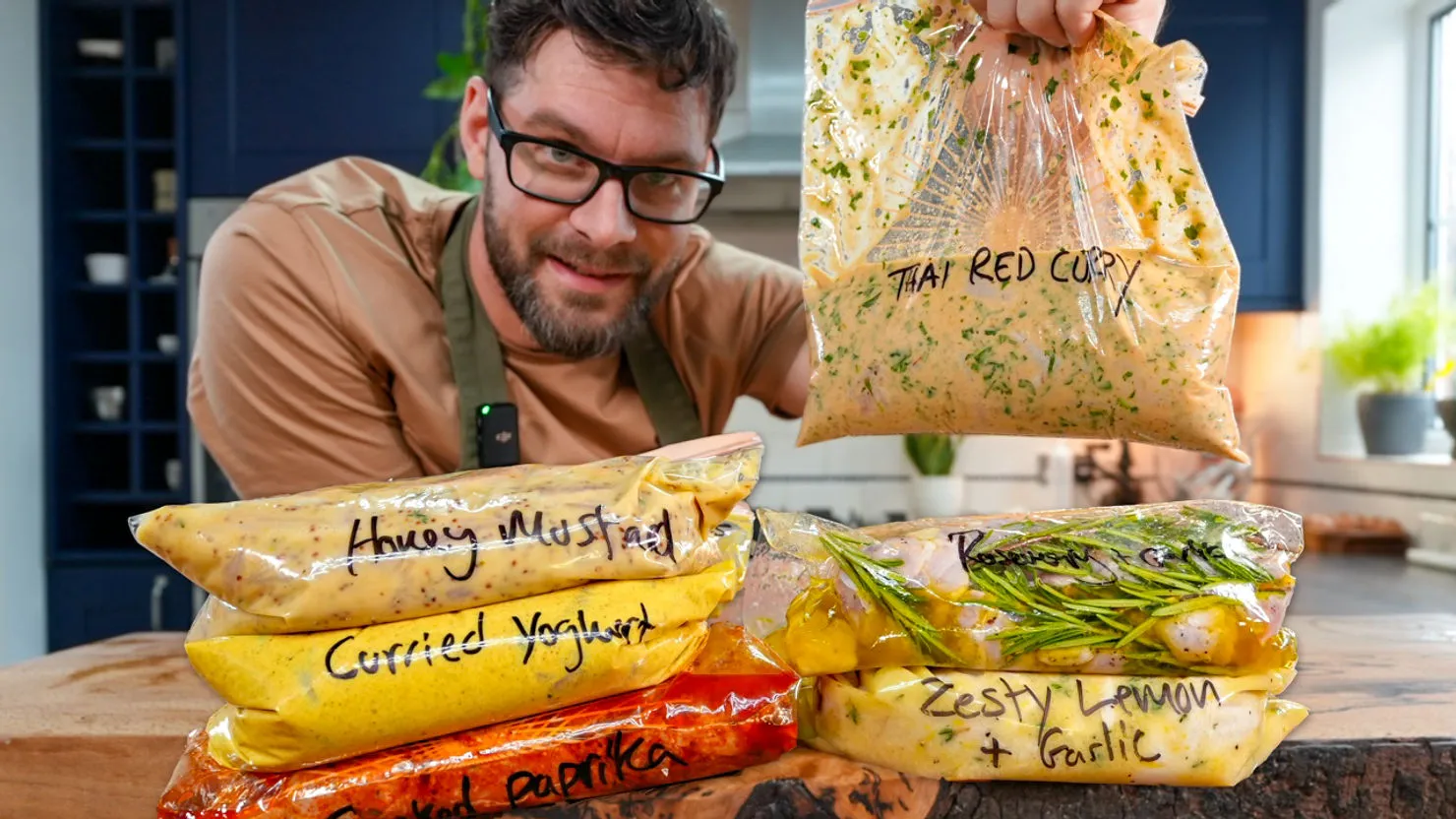 Man smiling, holding a bag labeled "Thai Red Curry." Other labeled bags with sauces on a wooden counter. Bright kitchen background.