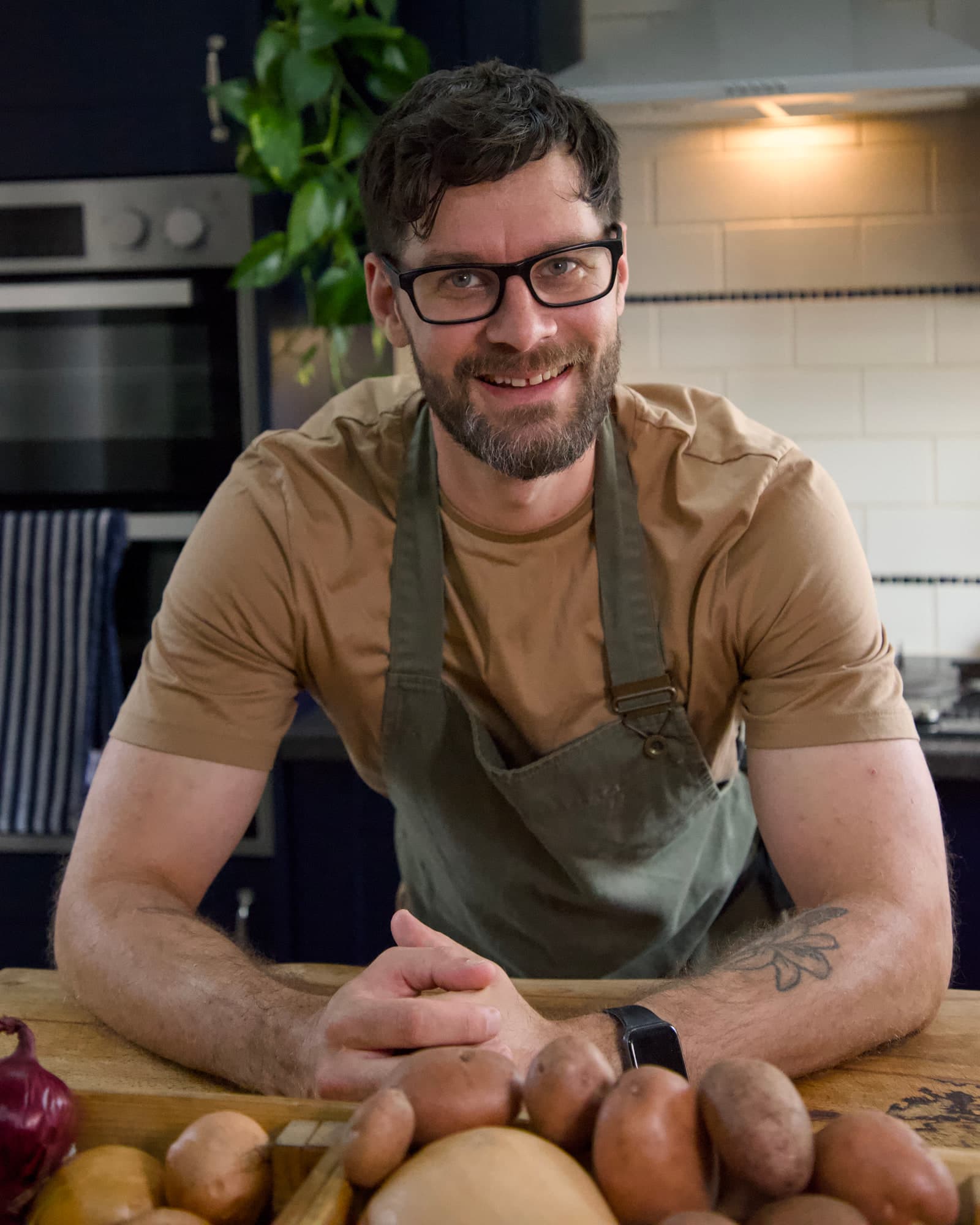 Tom resting his hands on a worktop laid with squash, potatoes and red onions