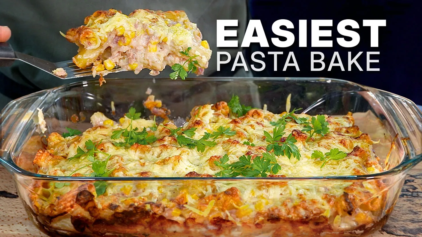 Glass dish of pasta bake with cheese and parsley garnish. A fork holds a serving. Text reads "EASIEST PASTA BAKE" in bold white.